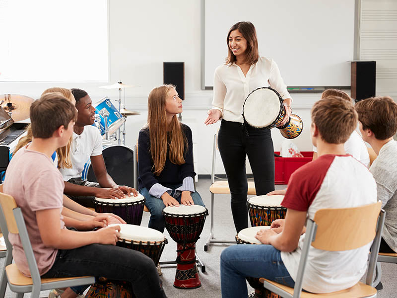 music teacher with circle of students playing djembe drums